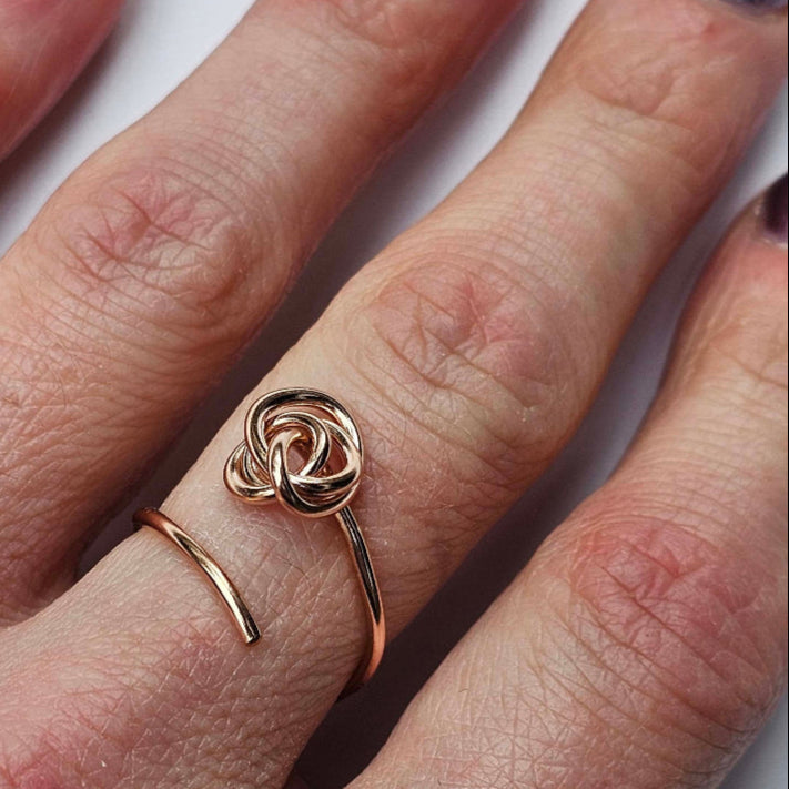 Woman's fingers wearing adjustable 14k Rose Gold knot ring on middle finger.