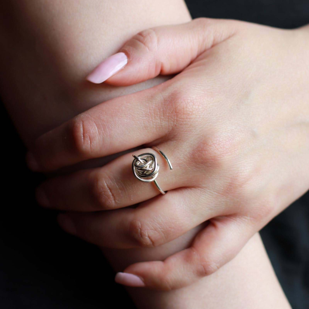 Woman's hand wearing an adjustable silver knot ring on her middle finger.