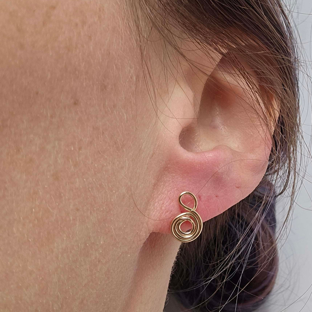 Gratitude Symbol Earrings in 14K Gold worn on a woman's earlobe with her hair tied back.
