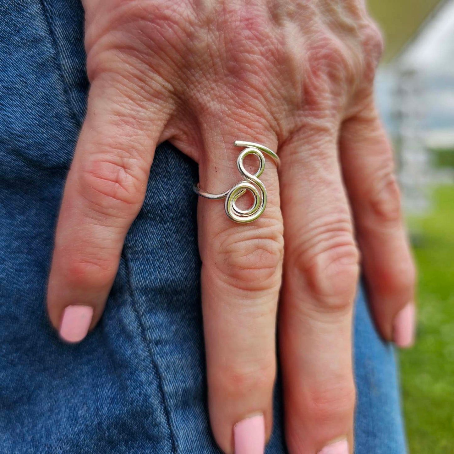 Silver adjustable gratitude ring worn on woman's index finger placed on jean pants.