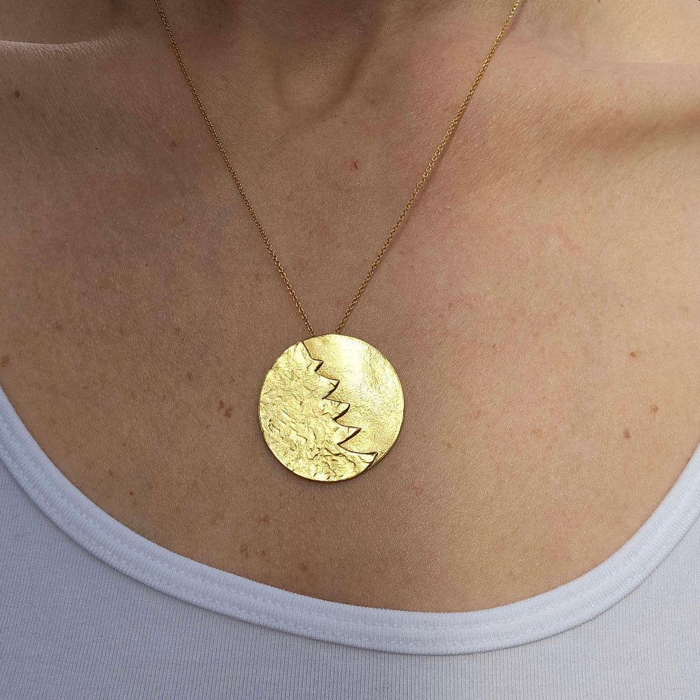 A woman wearing a gold Christmas necklace around her neck above a white shirt.