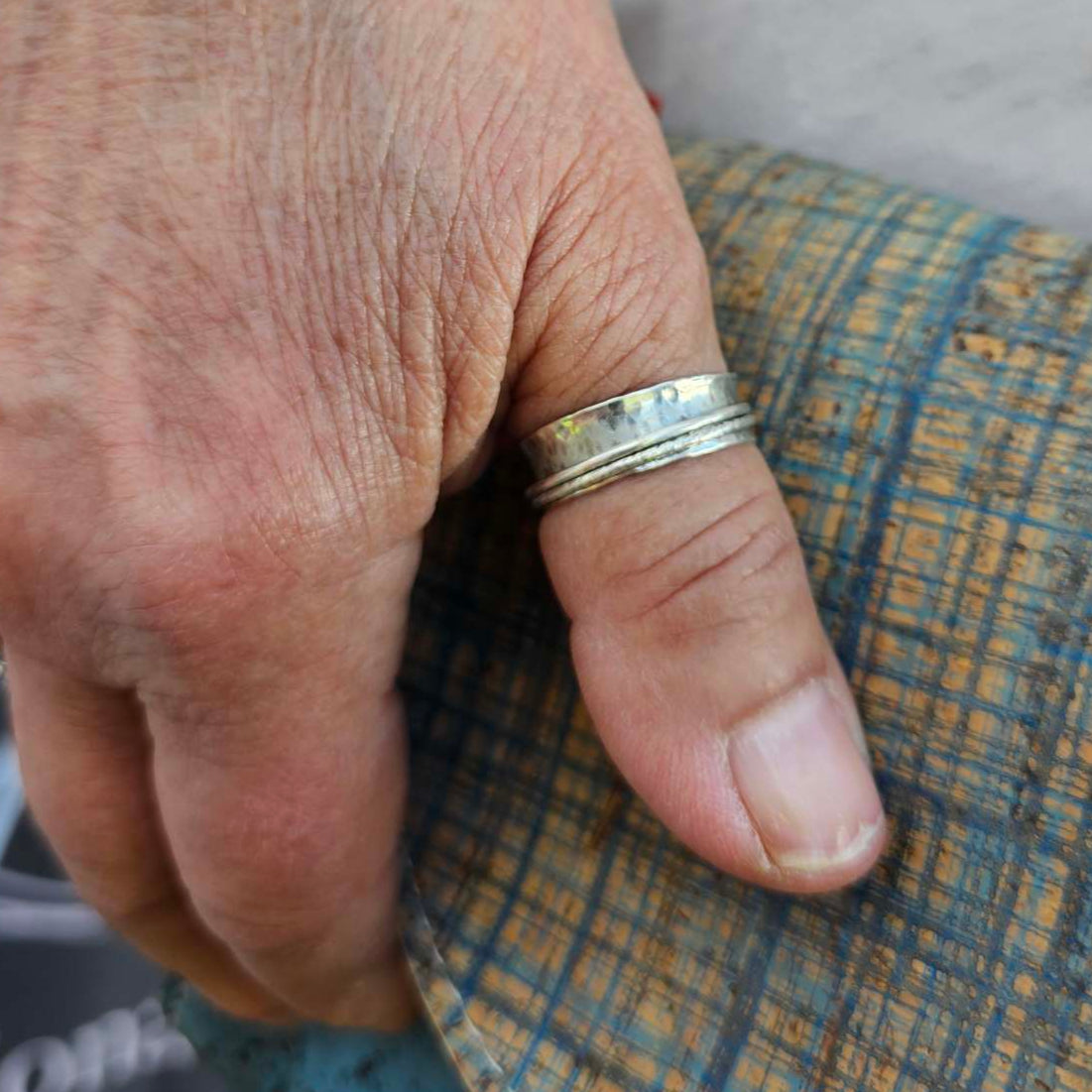 Woman's hand resting on bag wearing silver spinner ring for anxiety on her finger.