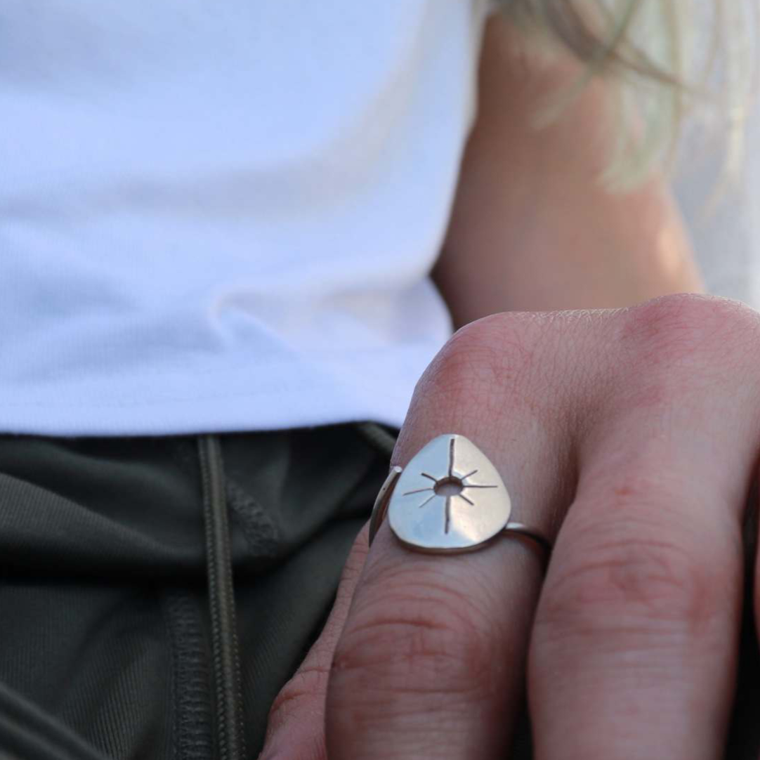 Silver ring worn on the pointer finger of a woman in a white shirt and green pants.