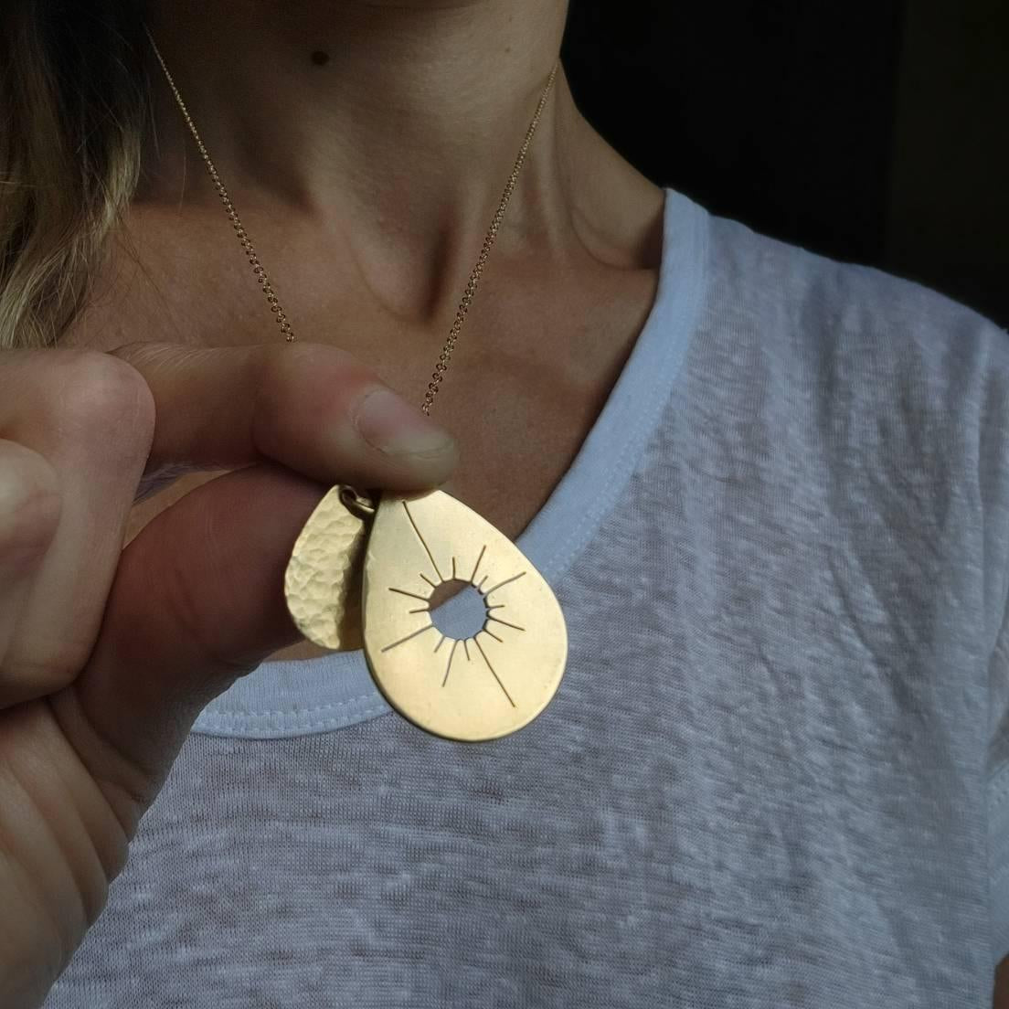 Woman wearing gold Sun Drop Necklace and holding it up between her fingers.