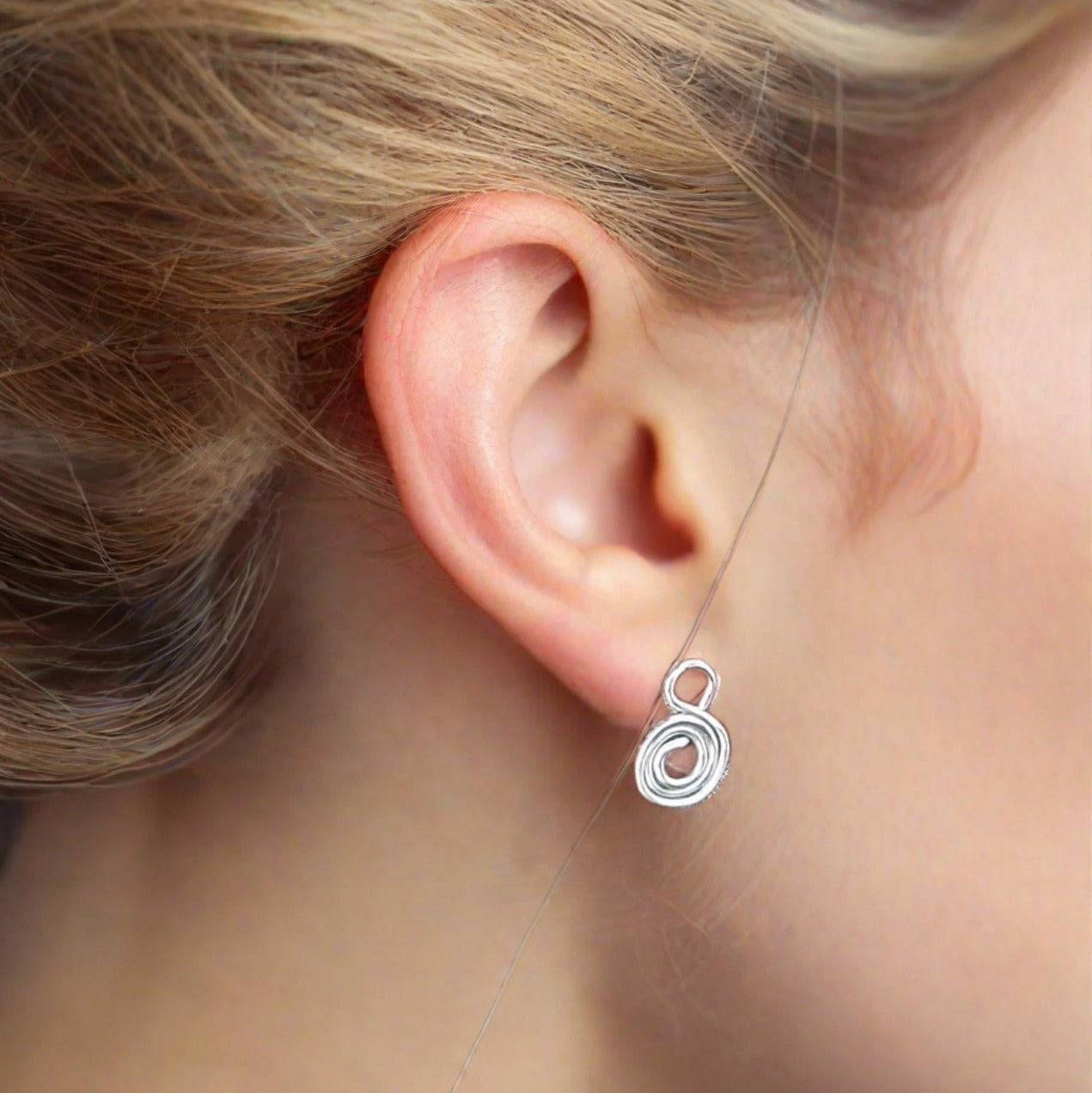 Gratitude Symbol silver stud Earrings on a woman's ear with her hair tied back.