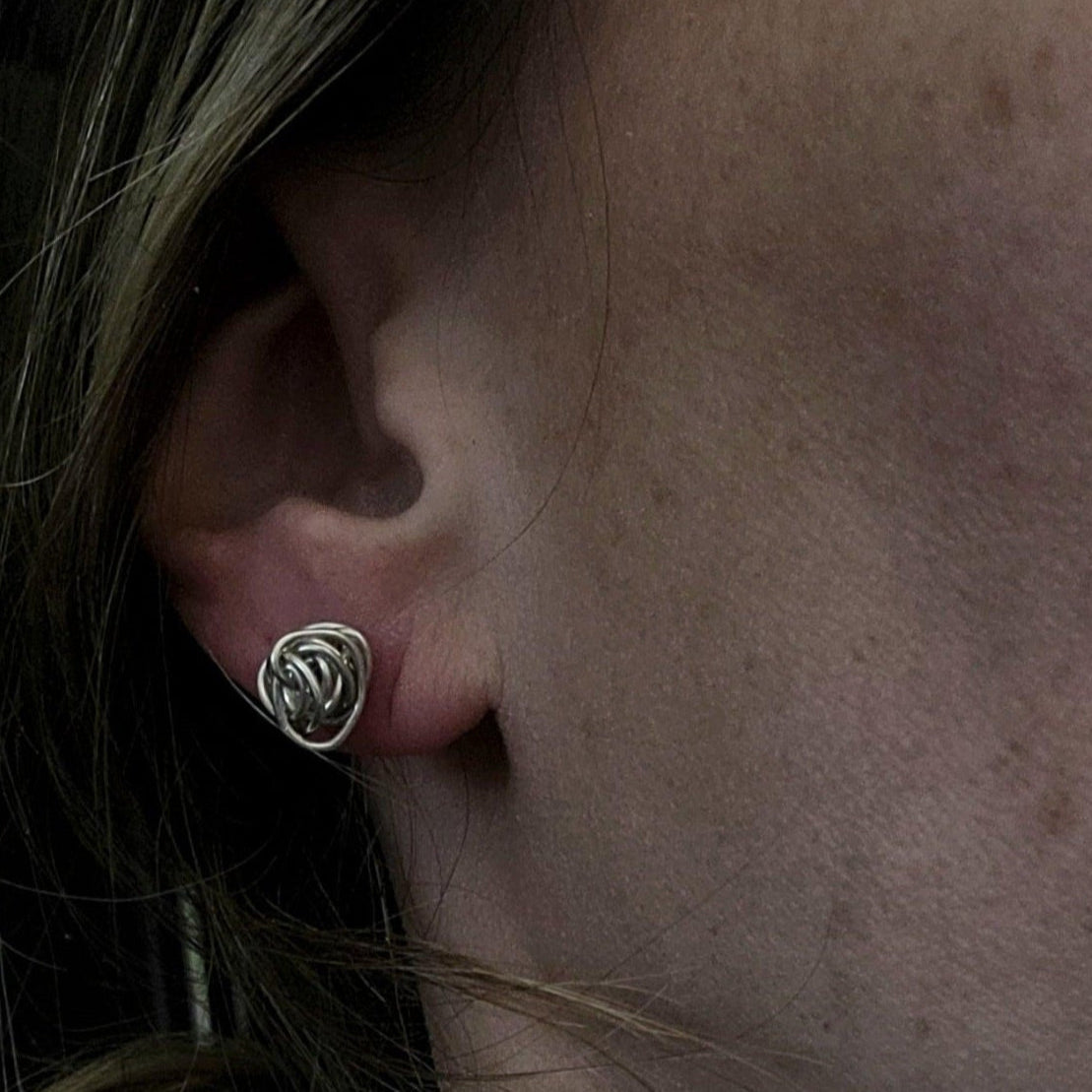 Woman wearing silver knot earring in her earlobe.