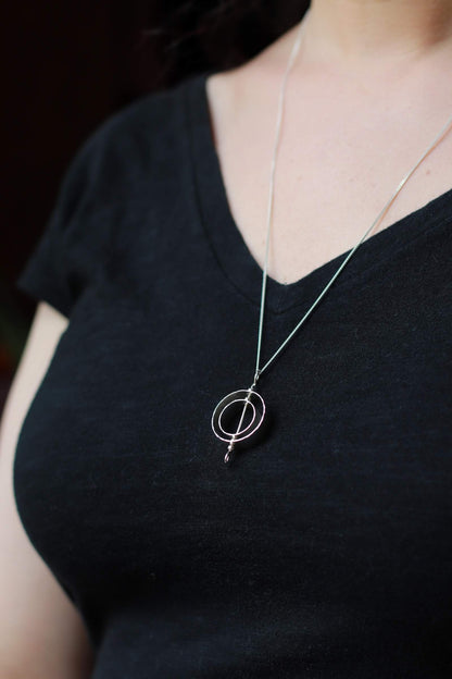 Karma necklace in sterling silver modeled on a woman in a black t-shirt.