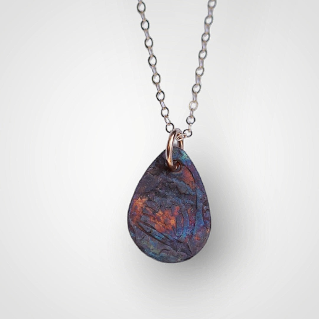 A unique copper necklace that reminds you to find beauty in unexpected places represented by the embossed designed and the colors elicited solely from the flame of the torch.