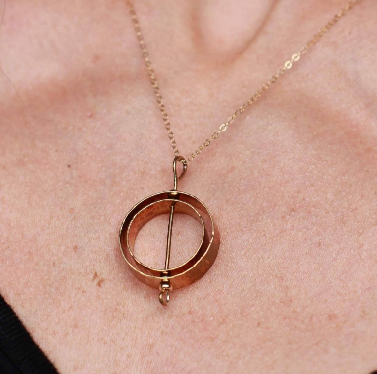 Gold Karma fidget necklace with 2 spinnable circles with a wire through the center on a chain worn on woman's neck.