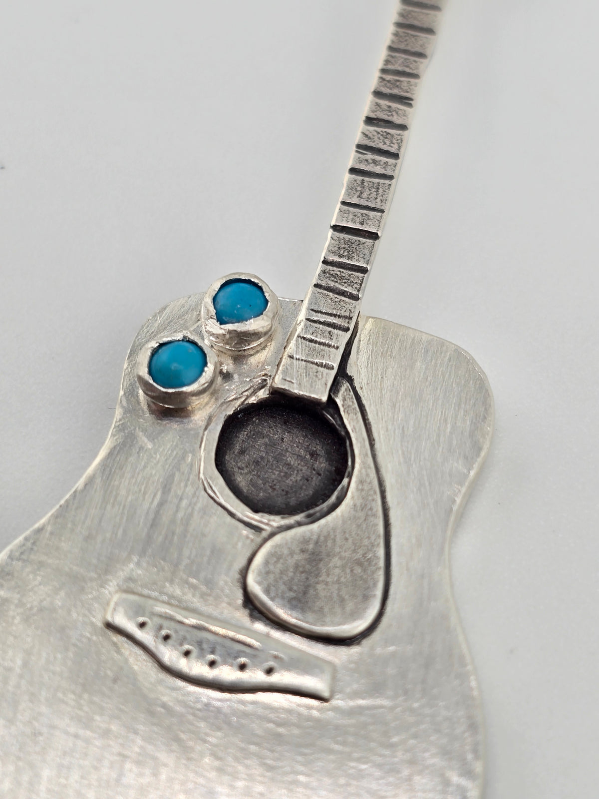 Close up of hand crafted guitar necklace on plain background. 