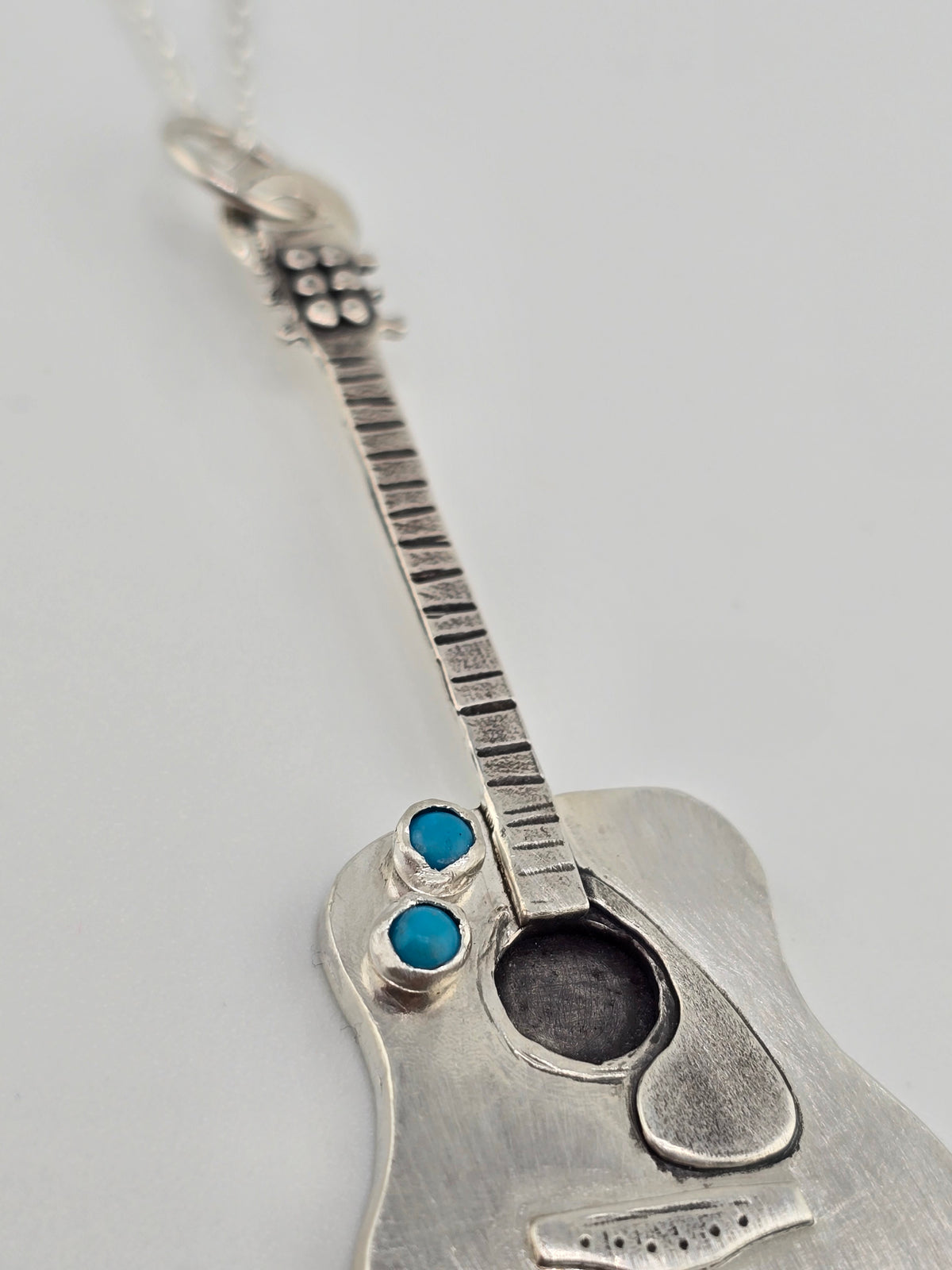 Close up of details of a guitar necklace on plain background.  
