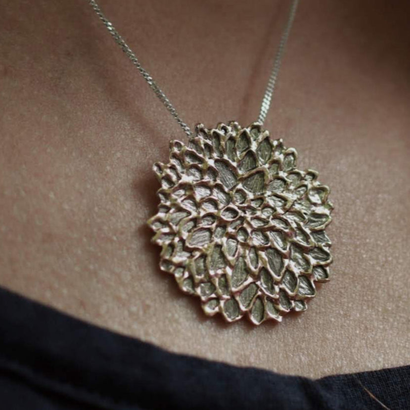 close up of custom jewelry dahlia pendant necklace on woman's neck with black shirt beneath