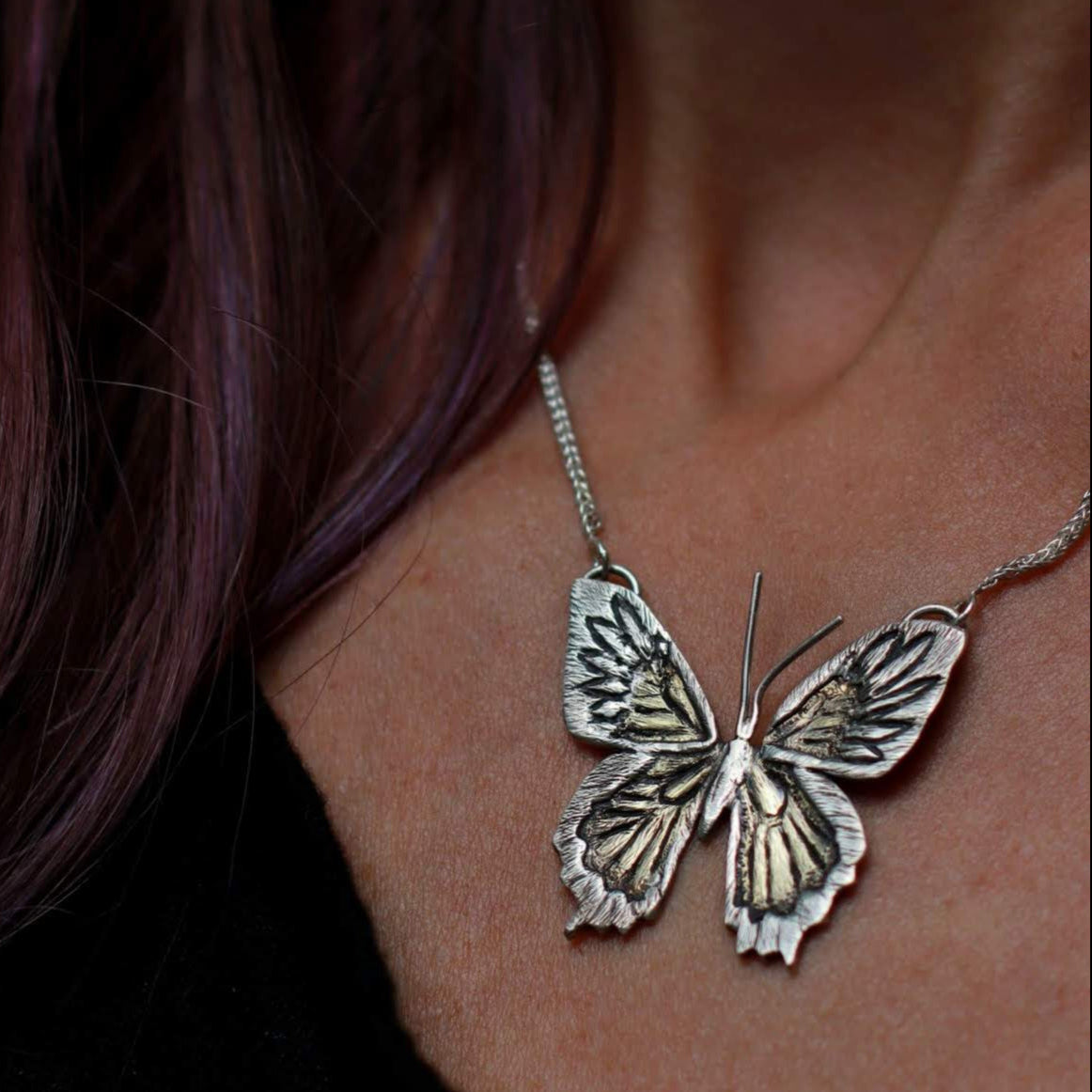 close up of handmade butterfly pendant necklace custom jewelry on woman's neck with black shirt.
