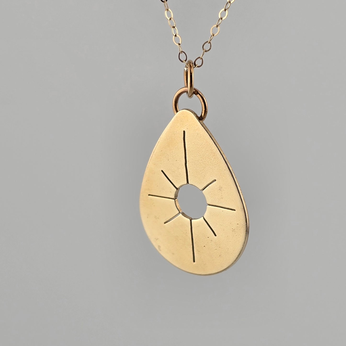 Gold teardrop pendant necklace on a gray background