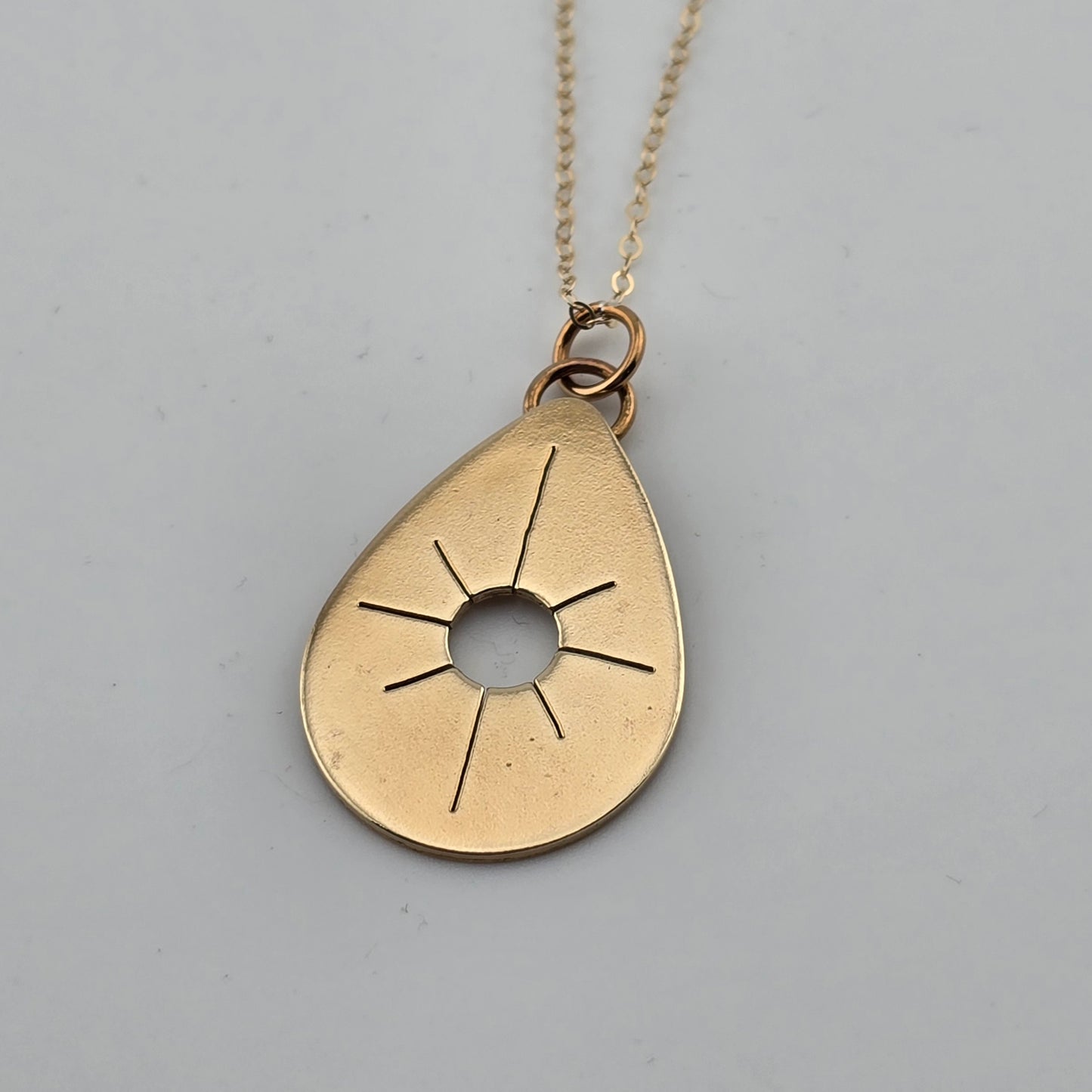 Gold teardrop-shaped pendant necklace on a gray background