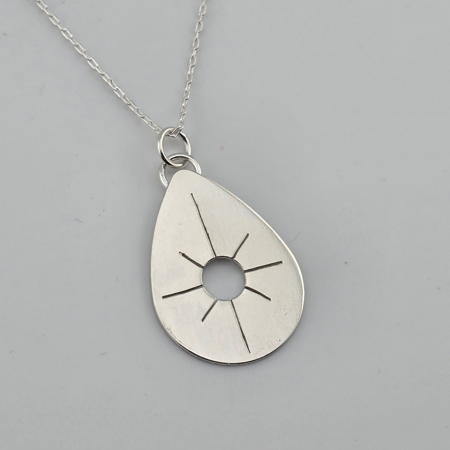 Silver teardrop pendant with sun design on a gray background