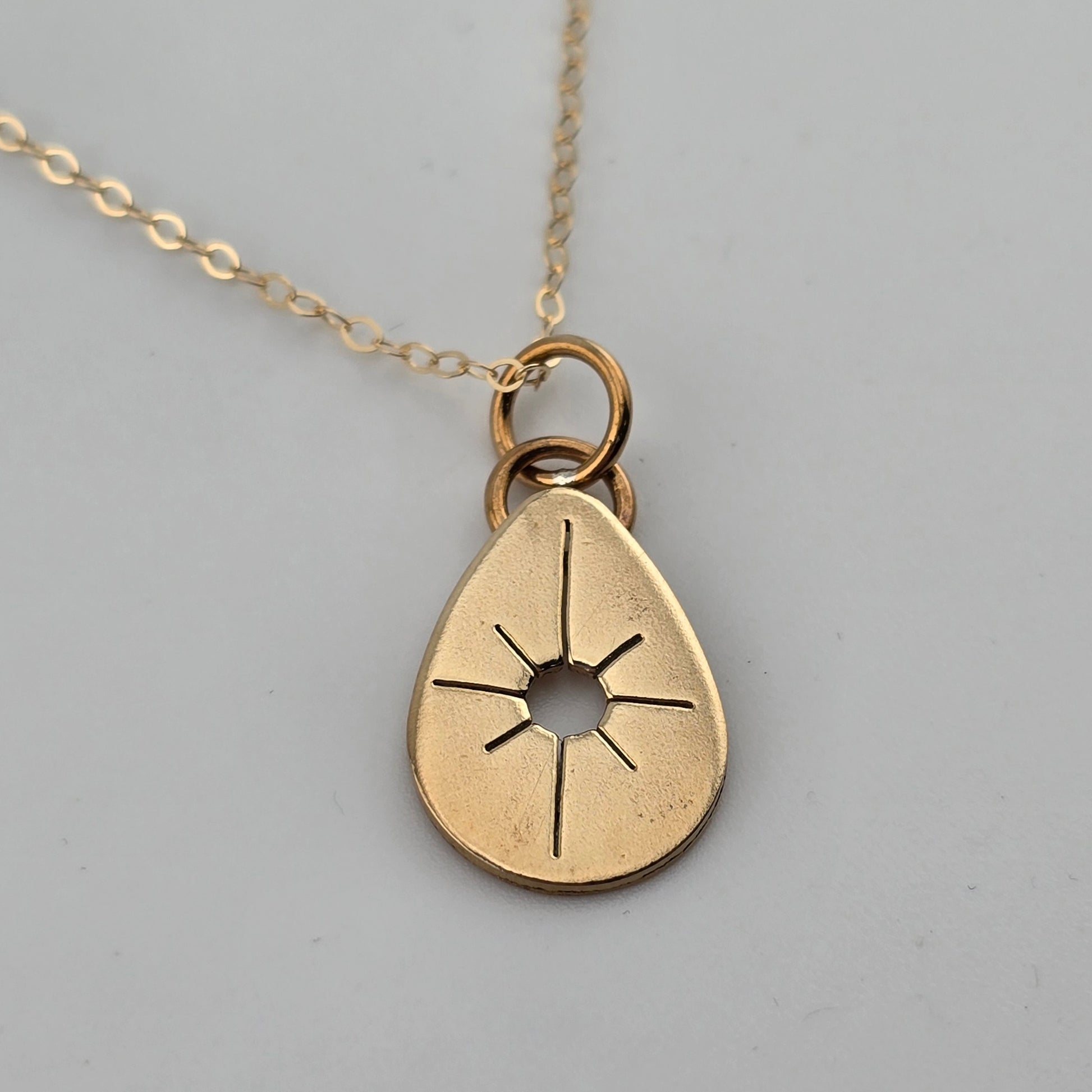 Gold teardrop-shaped pendant on a chain against a gray background
