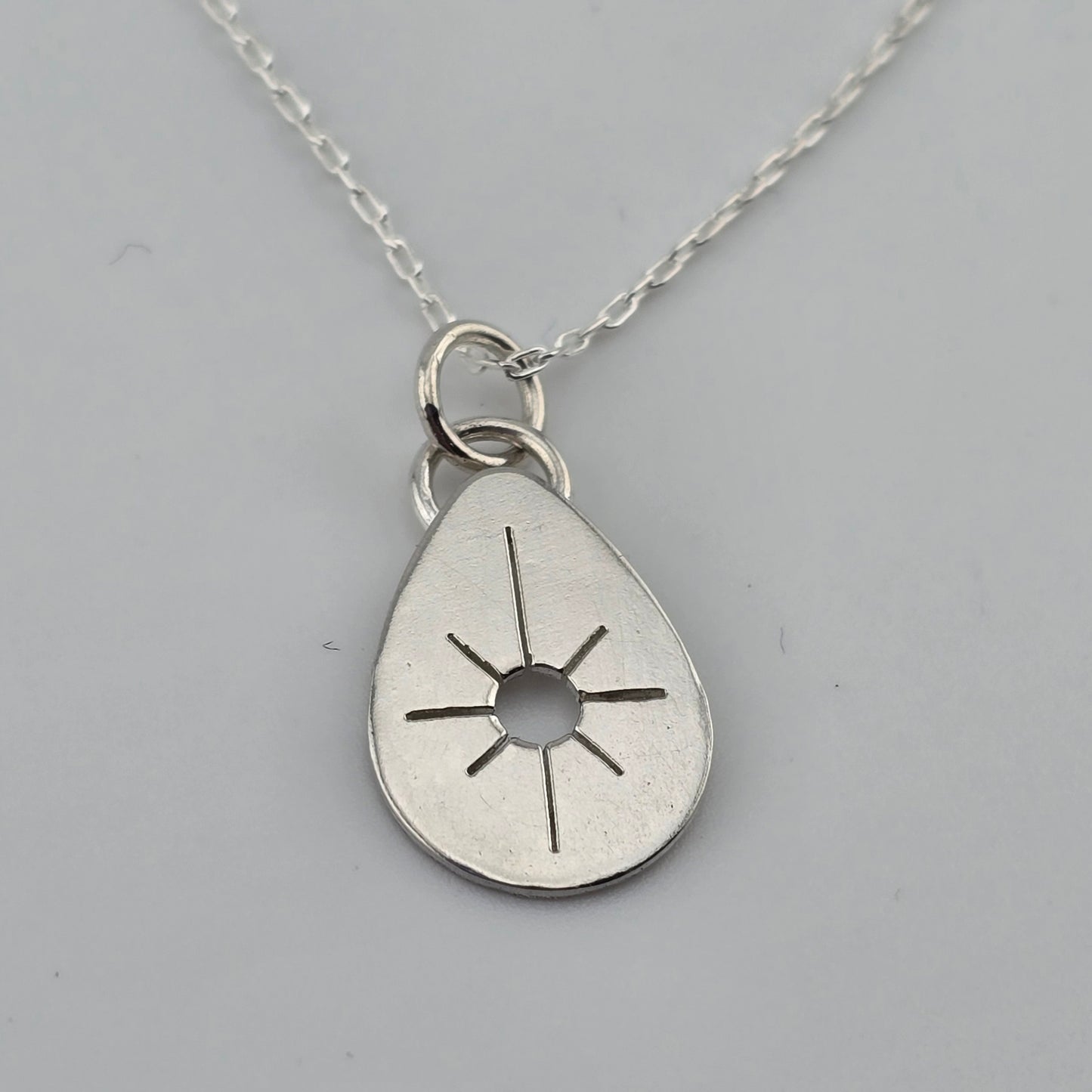 Silver teardrop pendant with sun design on a gray background