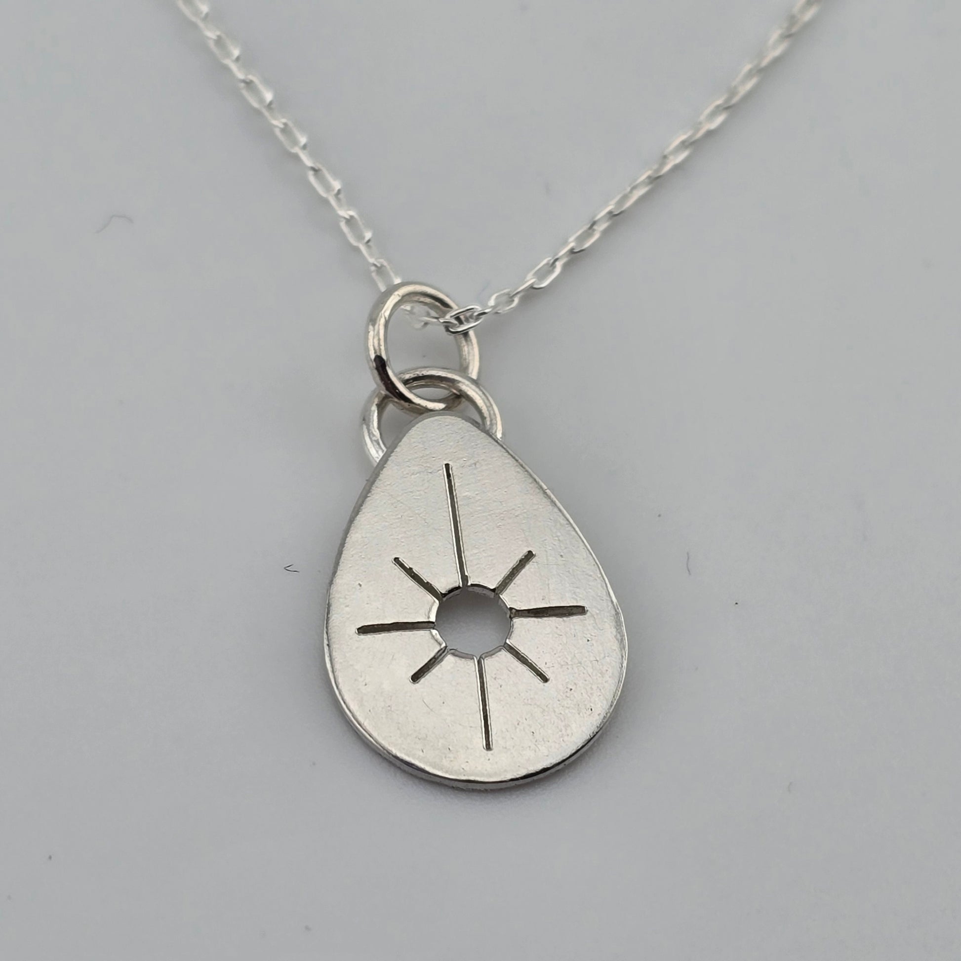 Silver teardrop pendant with sun design on a gray background