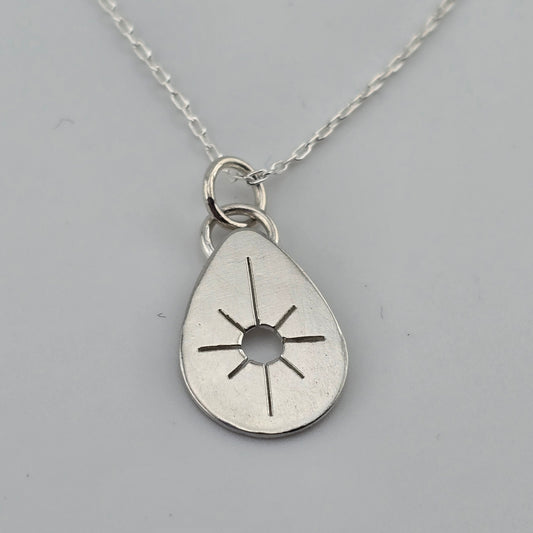 Silver teardrop pendant with sun design on a gray background