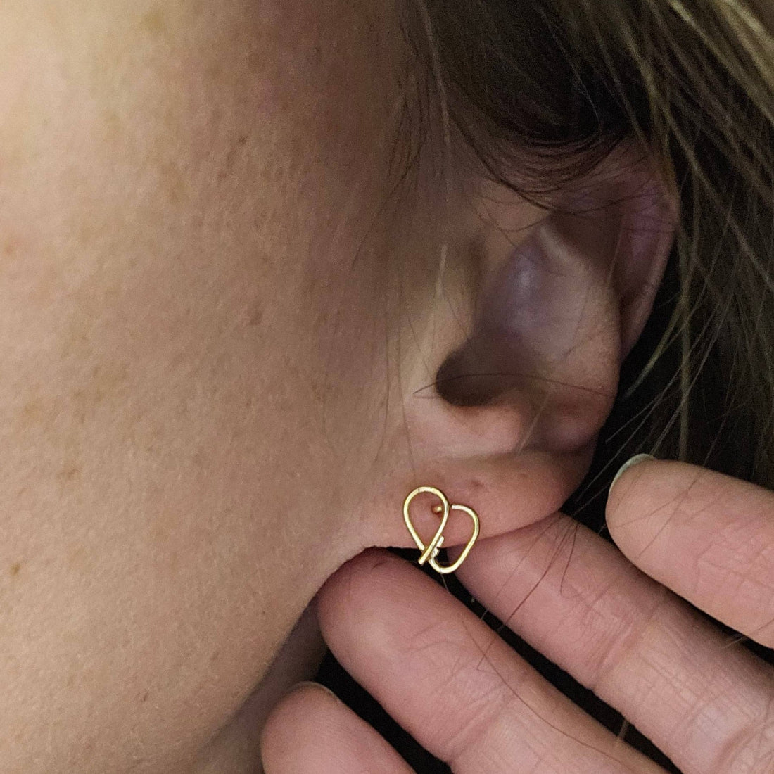 Self love key cute earrings in 14K Gold on a woman's ear with fingers behind ear.
