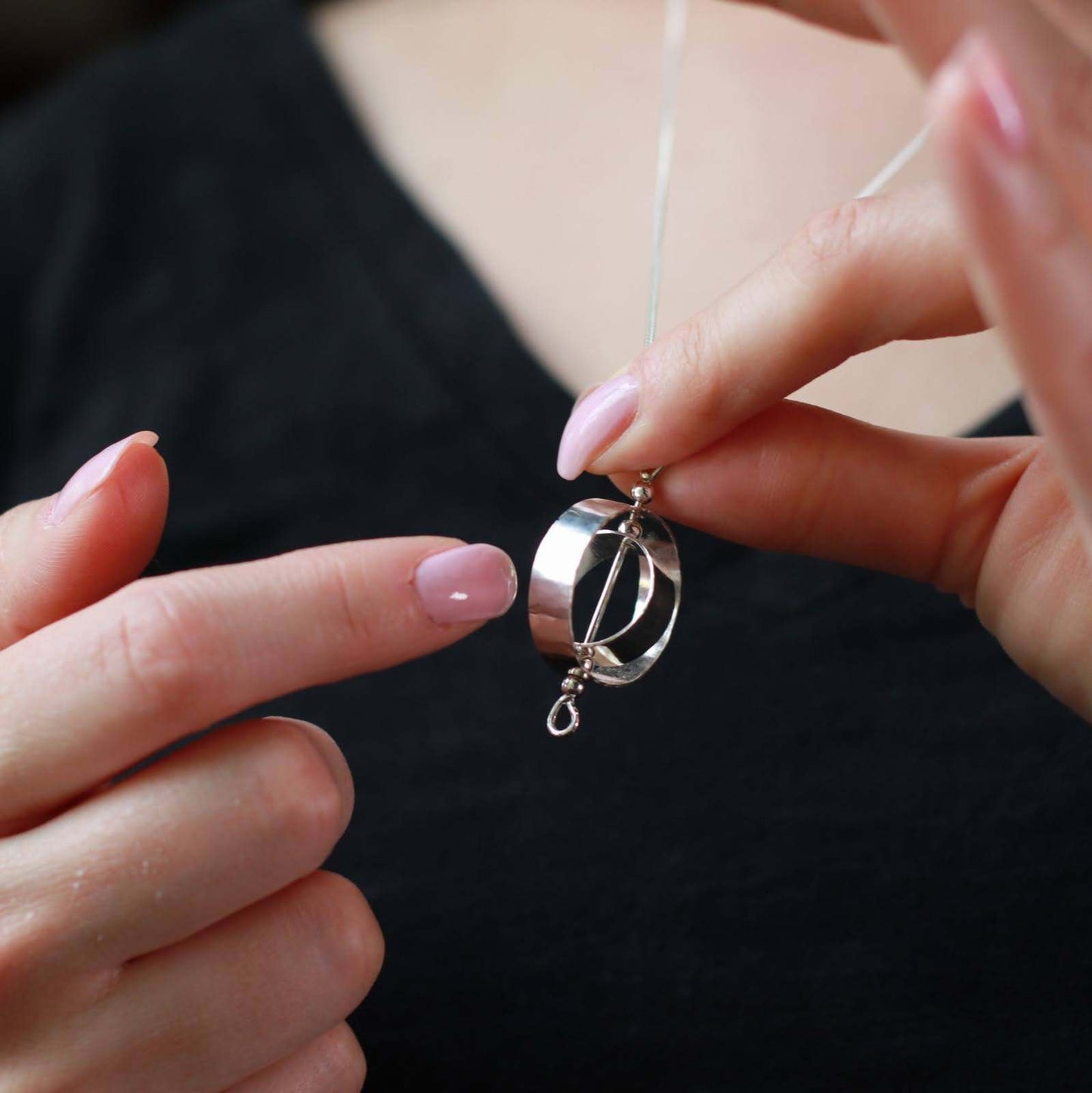 Woman holding silver fidget necklace for adults about to spin the circles with her finger.