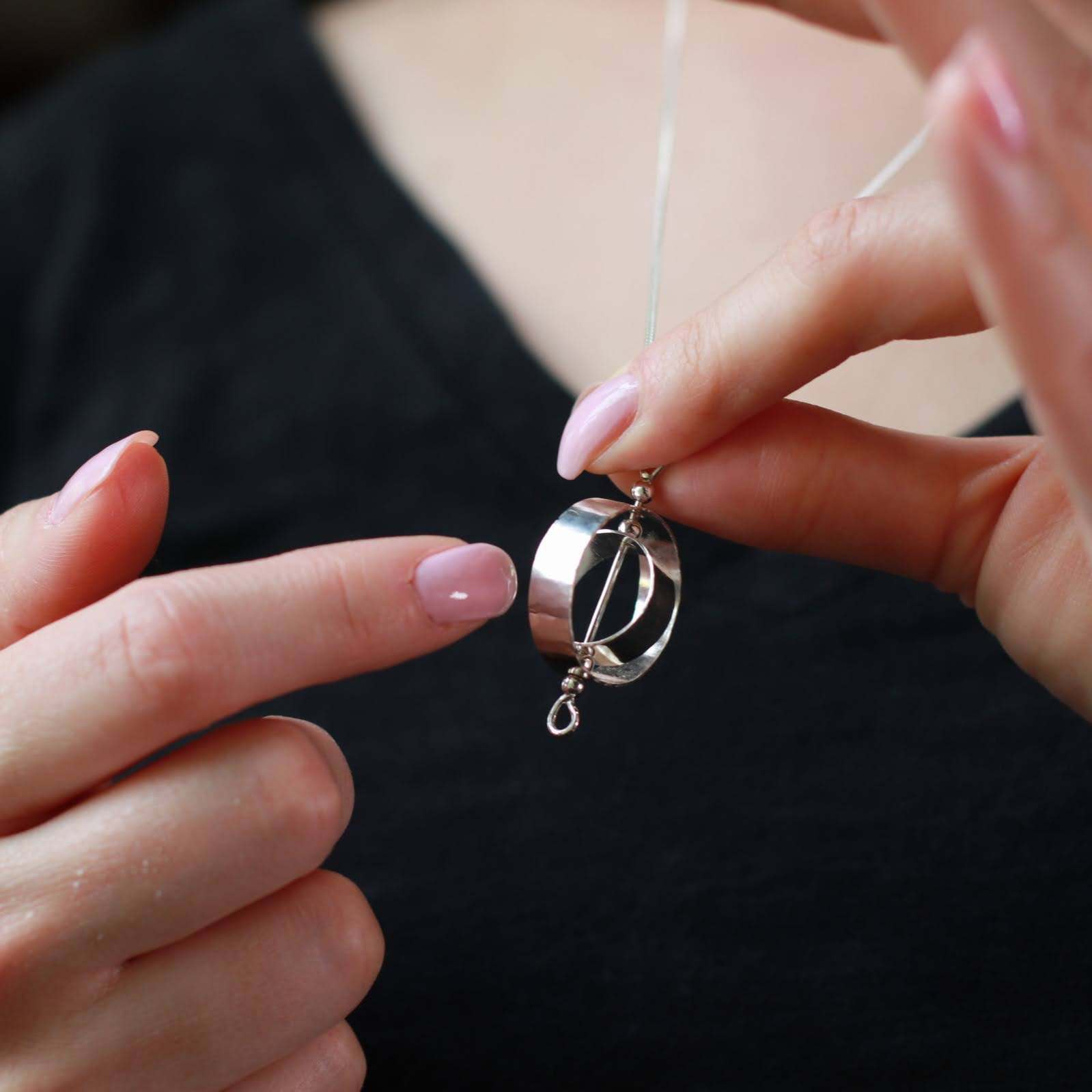 Woman holding silver fidget necklace for adults about to spin the circles with her finger.