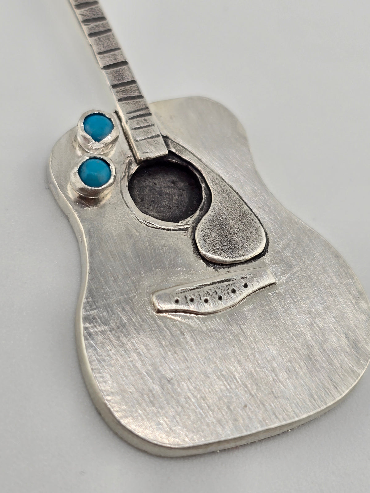 Close up of hand fabricated guitar necklace on plain background. 