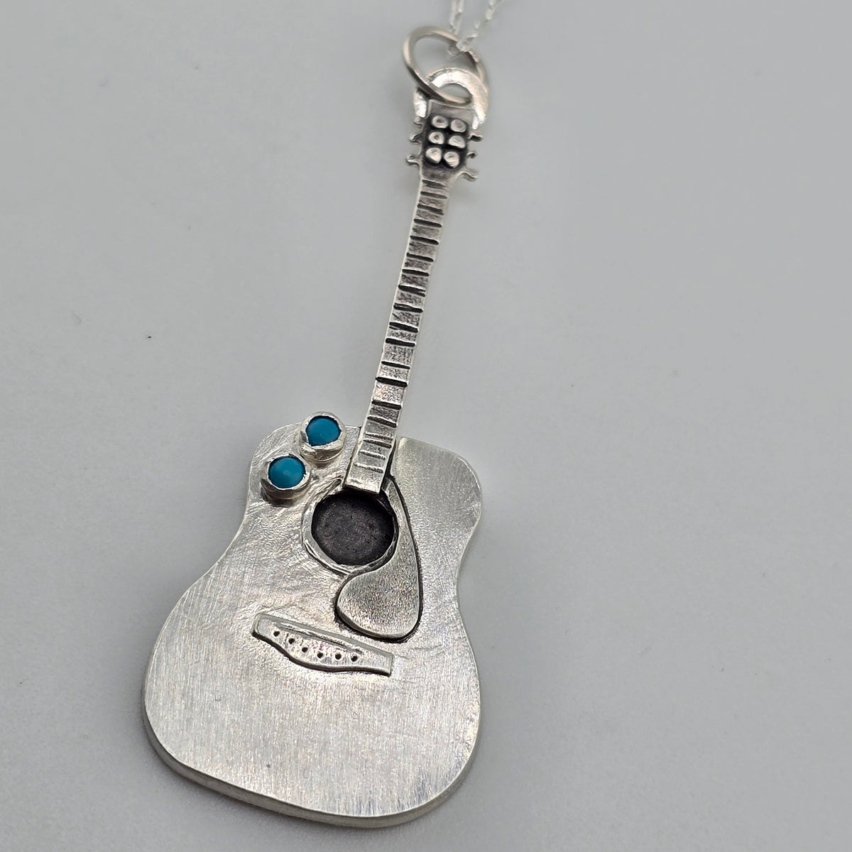 Handmade Silver Guitar Pendant on grey background