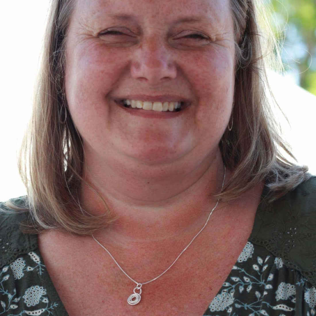 Smiling woman wearing a silver love and gratitude necklace handmade by Jaclyn Nicole