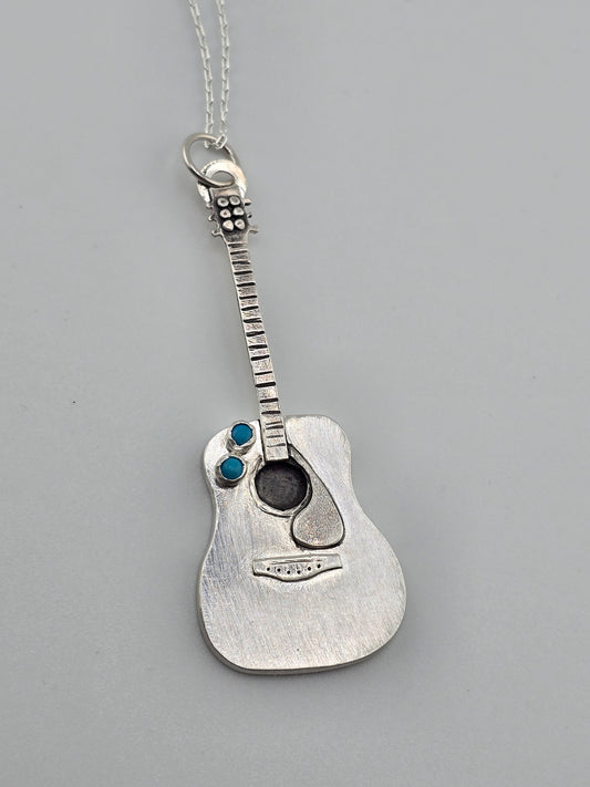 Close up shot of the details of a fully handmade silver guitar necklace with turquoise accent stones made by Jaclyn Nicole. 
