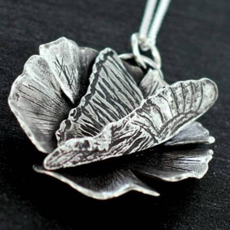 Hand fabricated silver pendant necklace of a butterfly landing on a flower with a silver chain attached.