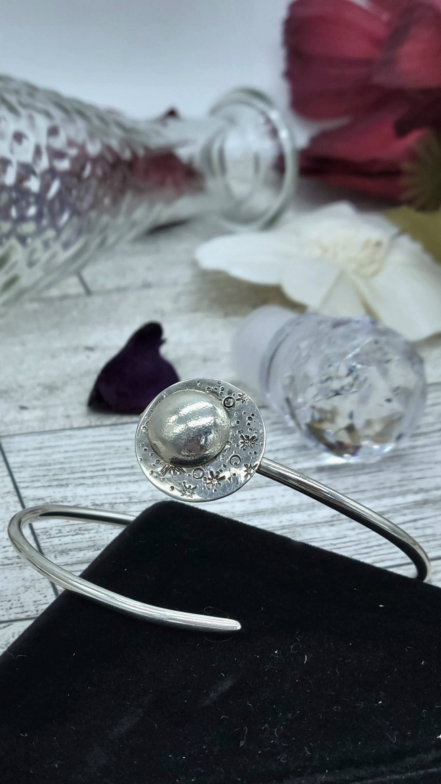 These sterling silver moon bracelets remind you to reflect on your prior successes to overcome present challenges - displayed with glass vase and flowers in the background.