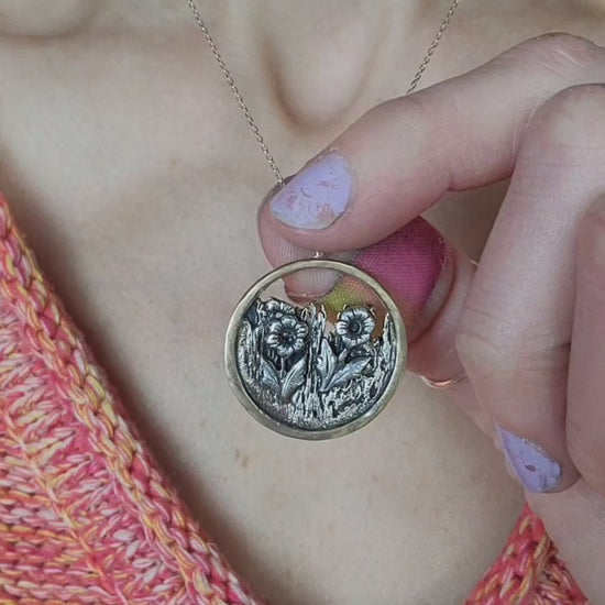 one-of-a-kind jewelry necklace held between woman's fingers with an orange sweater
