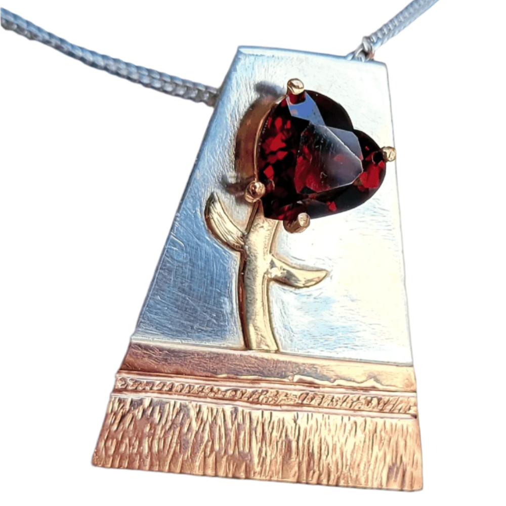 close up of handmade  custom jewelry necklace with garnet heart shaped "flower" in a "pot" fabricated with  silver, 14k gold and 14k rose gold.