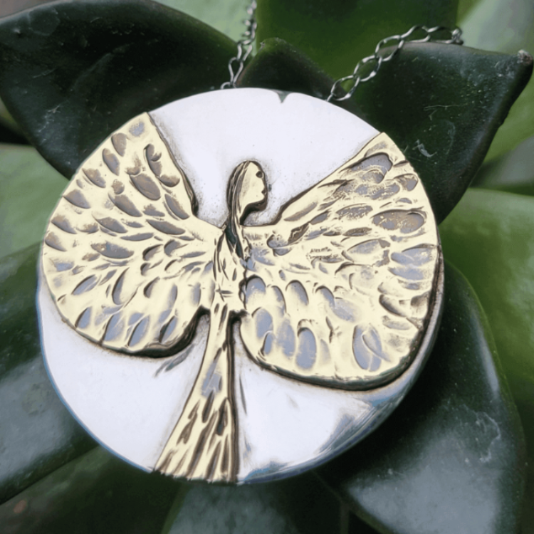 Silver and gold angel necklace atop a green succulent plant